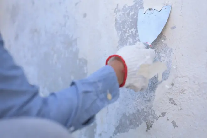 How to Remove Paint From a Home’s Exterior 1 Person applying plaster to a wall with a trowel.