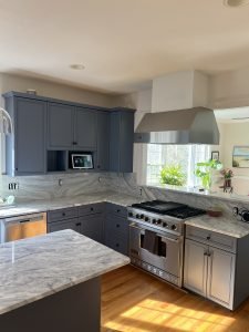 Blog 18 A modern kitchen with stainless steel appliances and gray cabinetry, featuring marble countertops and ample natural light.
