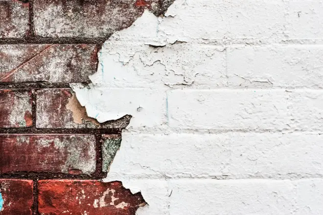 How to Remove Paint From a Home’s Exterior 2 Peeling white paint on a brick wall reveals underlying red bricks.